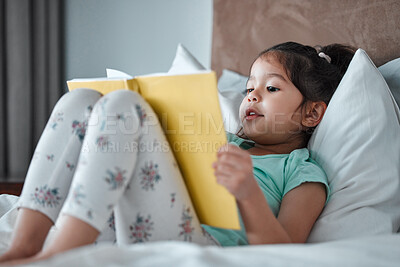 Buy stock photo Shot of a little girl reading a book while lying on her bed