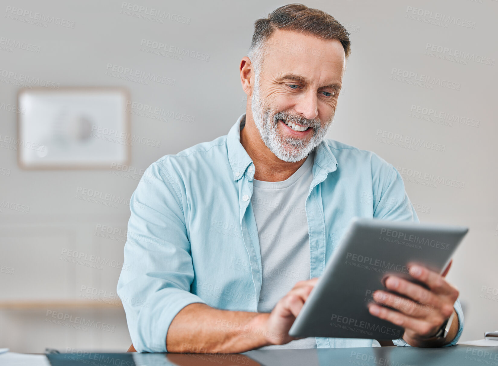 Buy stock photo Shot of a mature businessman sitting alone in his office and using a digital tablet