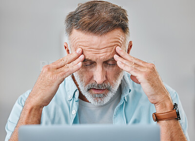 Buy stock photo Shot of a mature businessman sitting alone in his office and suffering from a headache while using his laptop