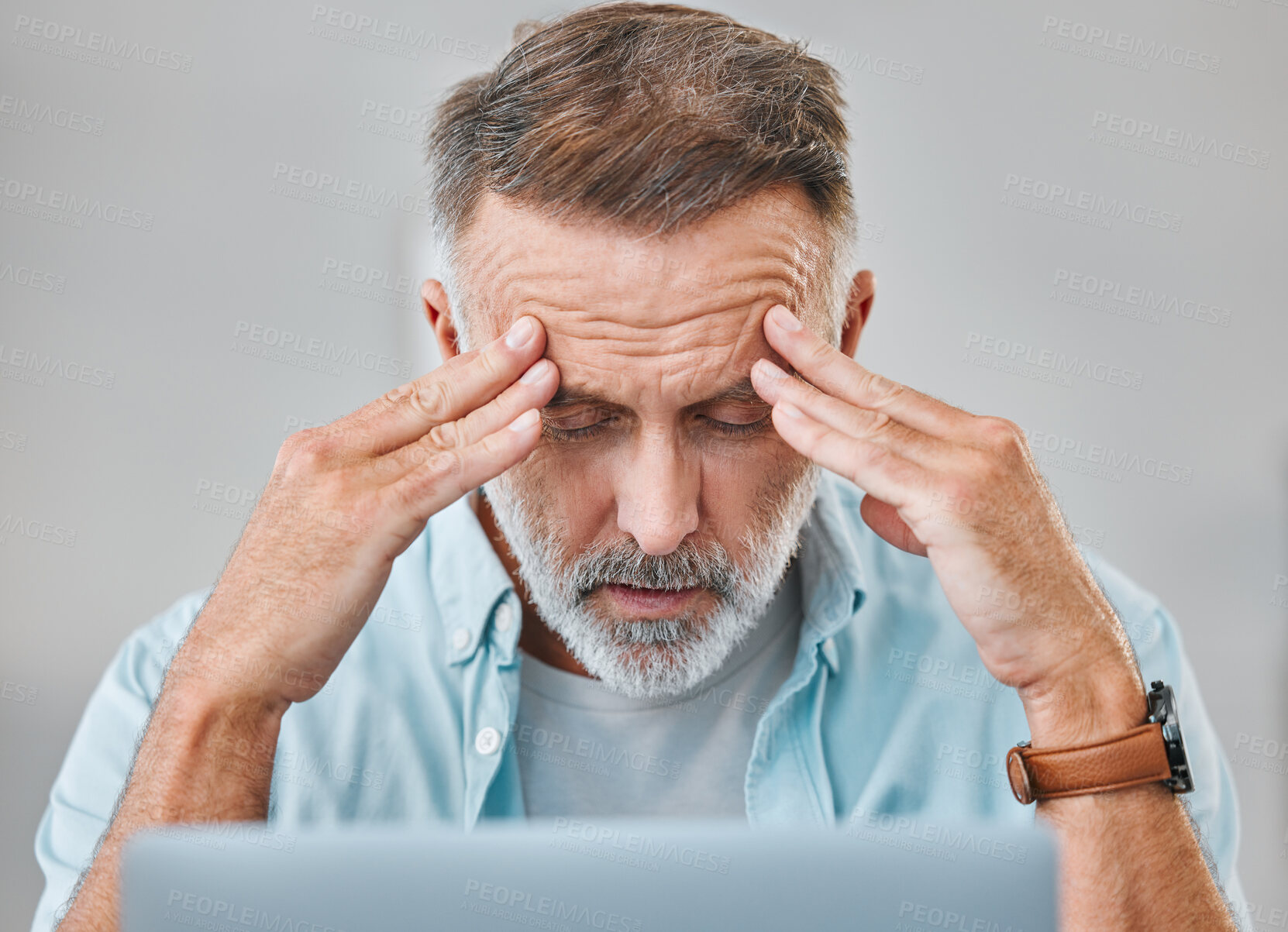 Buy stock photo Shot of a mature businessman sitting alone in his office and suffering from a headache while using his laptop