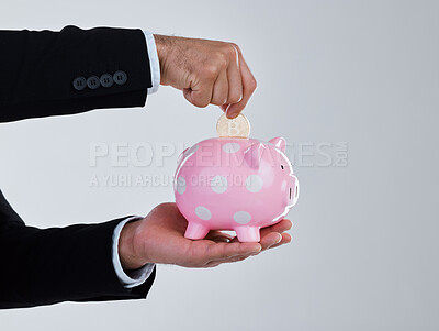 Buy stock photo Shot of an unrecognizable businessman depositing coins into his piggy bank against a grey background