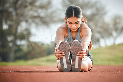 Buy stock photo Shot of a young athlete stretching her legs on a running track outdoors