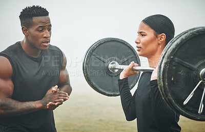 Buy stock photo Shot of a sporty young woman exercising with a barbell with the help of a trainer outdoors