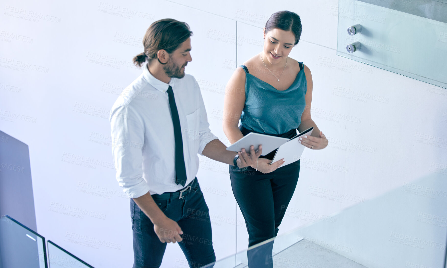 Buy stock photo Shot of two coworkers walking through their office while using a digital tablet and talking