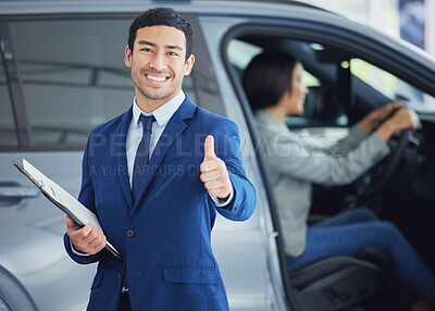 Buy stock photo Cropped portrait of a handsome young male car salesman giving thumbs up on the showroom floor with a female customer in a vehicle behind him