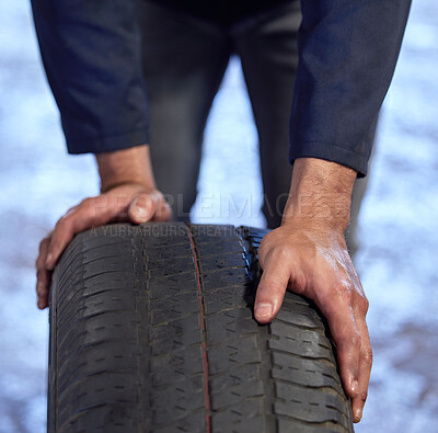 Buy stock photo High angle shot of an unrecognizable male mechanic rolling a tyre through his workshop during a service