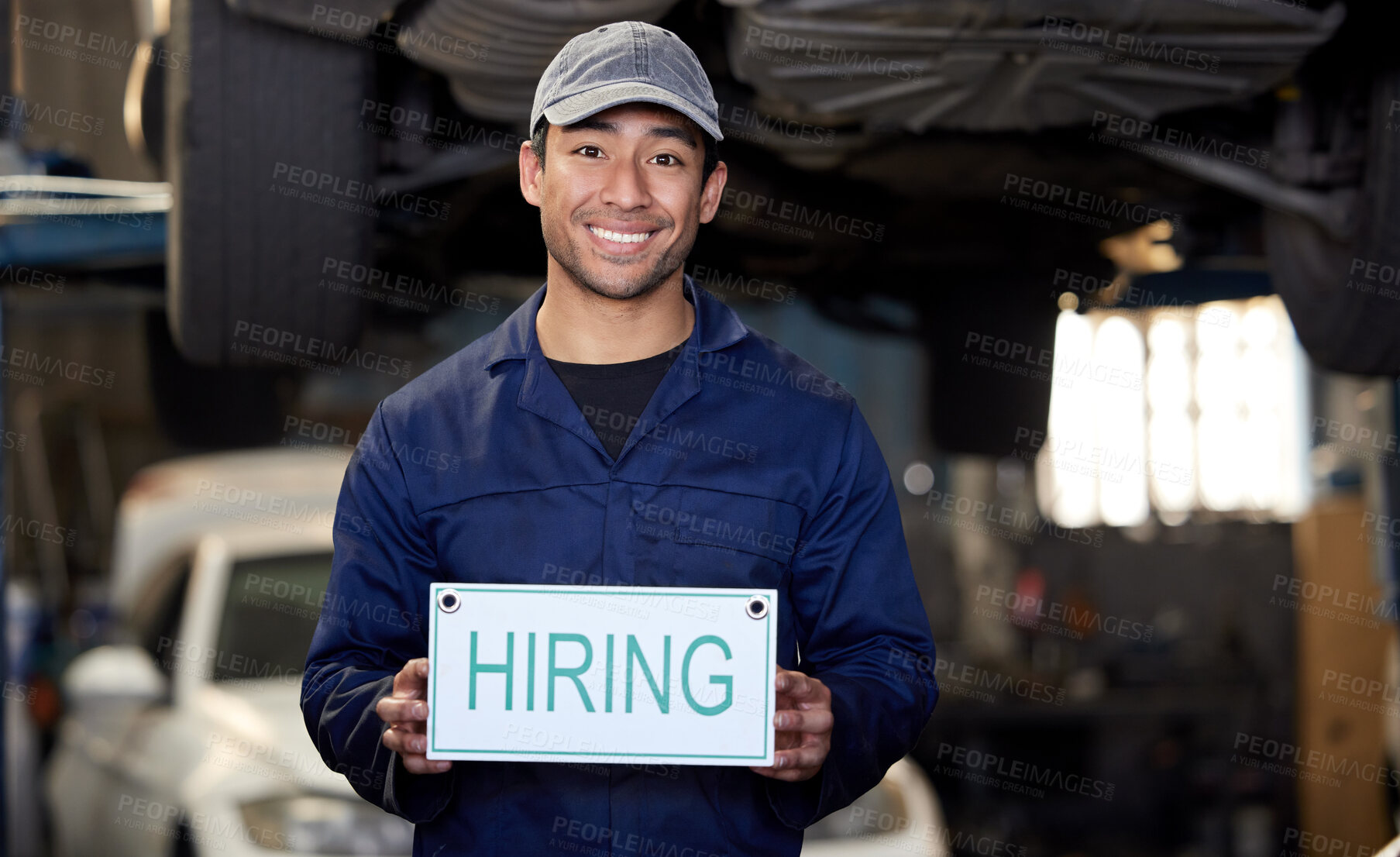 Buy stock photo Cropped portrait of a handsome young male mechanic holding a hiring sign while standing in his workshop