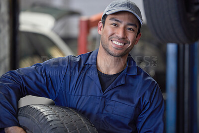 Buy stock photo Cropped portrait of a handsome young male mechanic carrying a tyre through his workshop