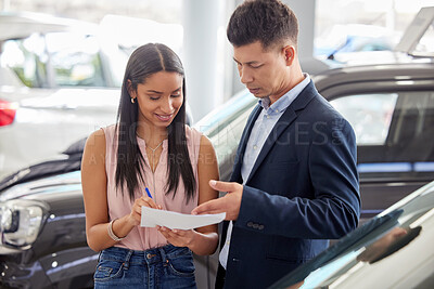 Buy stock photo Shot of a young woman signing paperwork at a car dealership