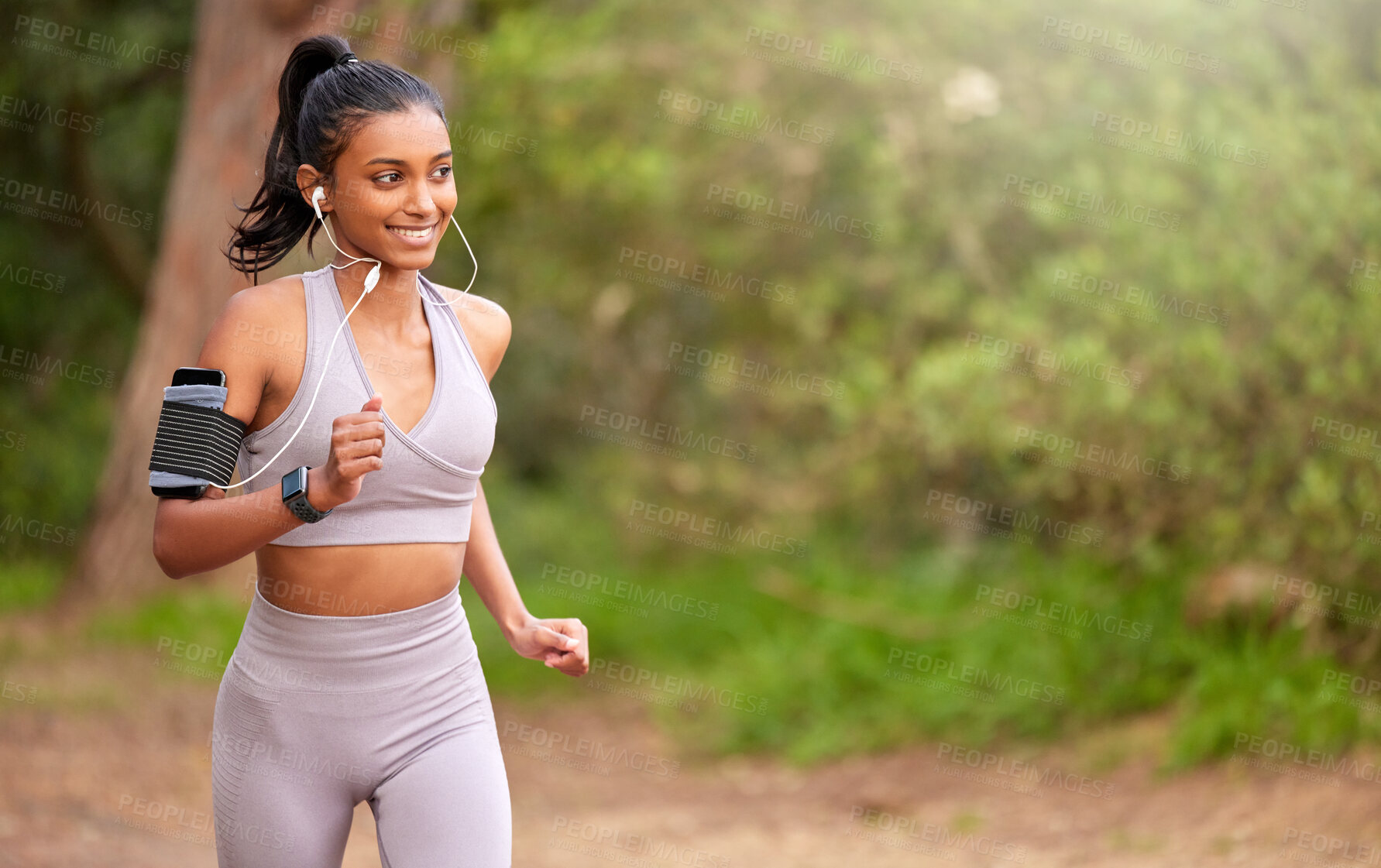 Buy stock photo Shot of a young woman jogging and listening to music while making her way through a forest