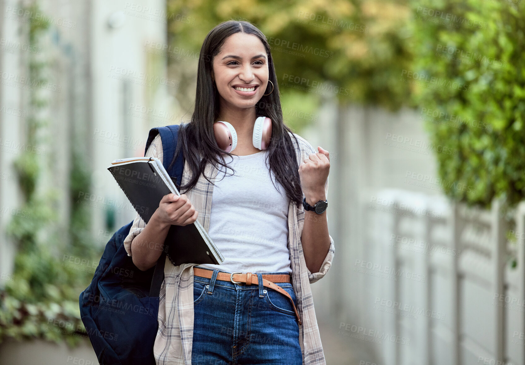 Buy stock photo Student, girl and fist pump on campus with smile, headphones and books for learning, development and study. Female person, happy and university for class, course and success in exam for education