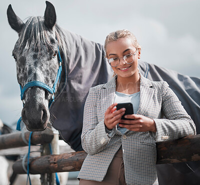 Buy stock photo Shot of an attractive woman using her cellphone while posing with a horse in an enclosed pasture on a farm