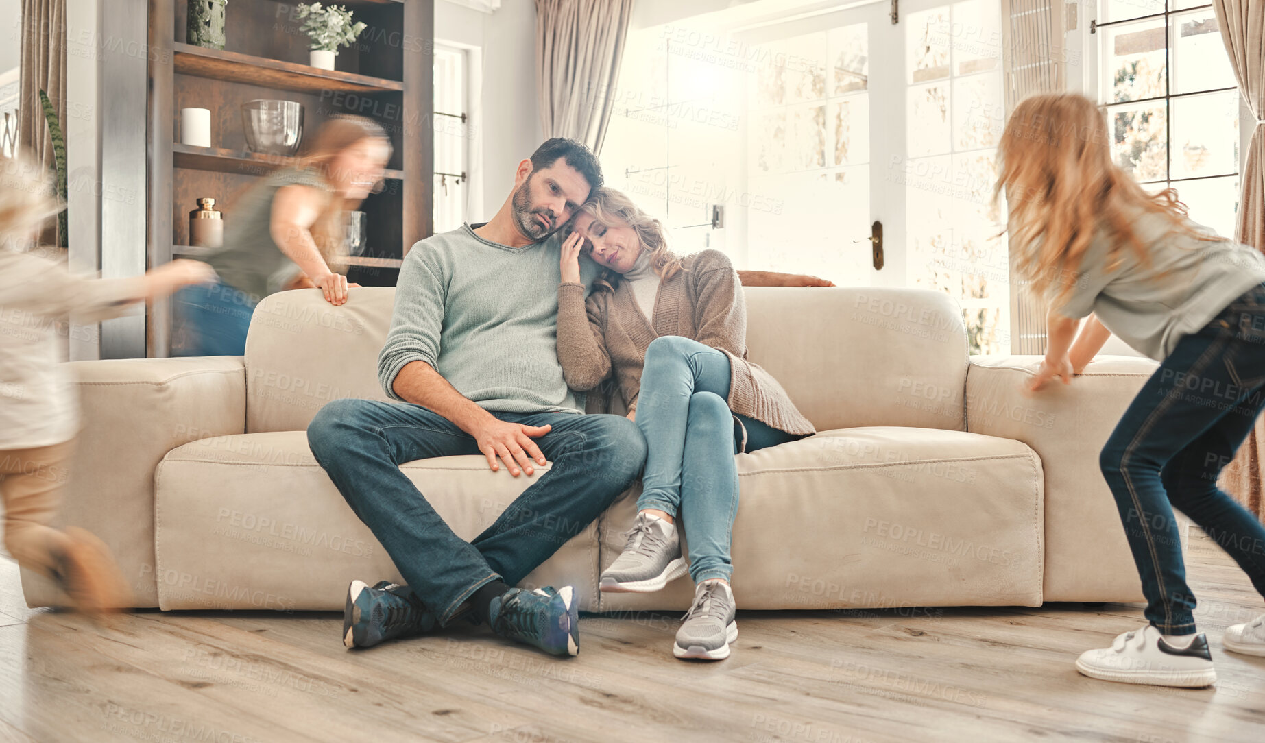 Buy stock photo ADHD, children running and exhausted parents on sofa in living room of home with anxiety or stress.  Autism, energy or noise with resting mom and tired dad watching excited kids in apartment together