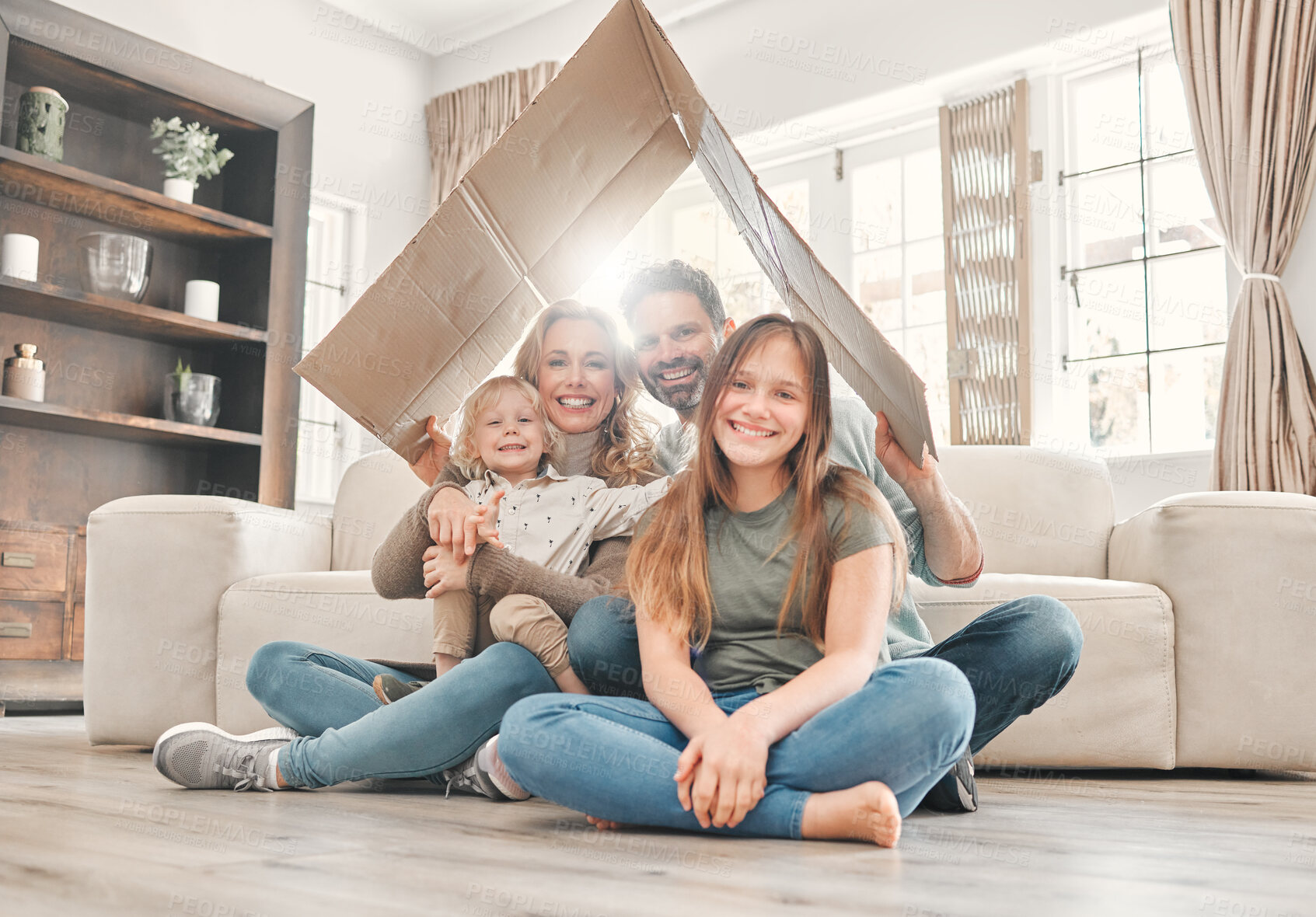 Buy stock photo Shot of a young family holding up a cardboard box to form a roof at home