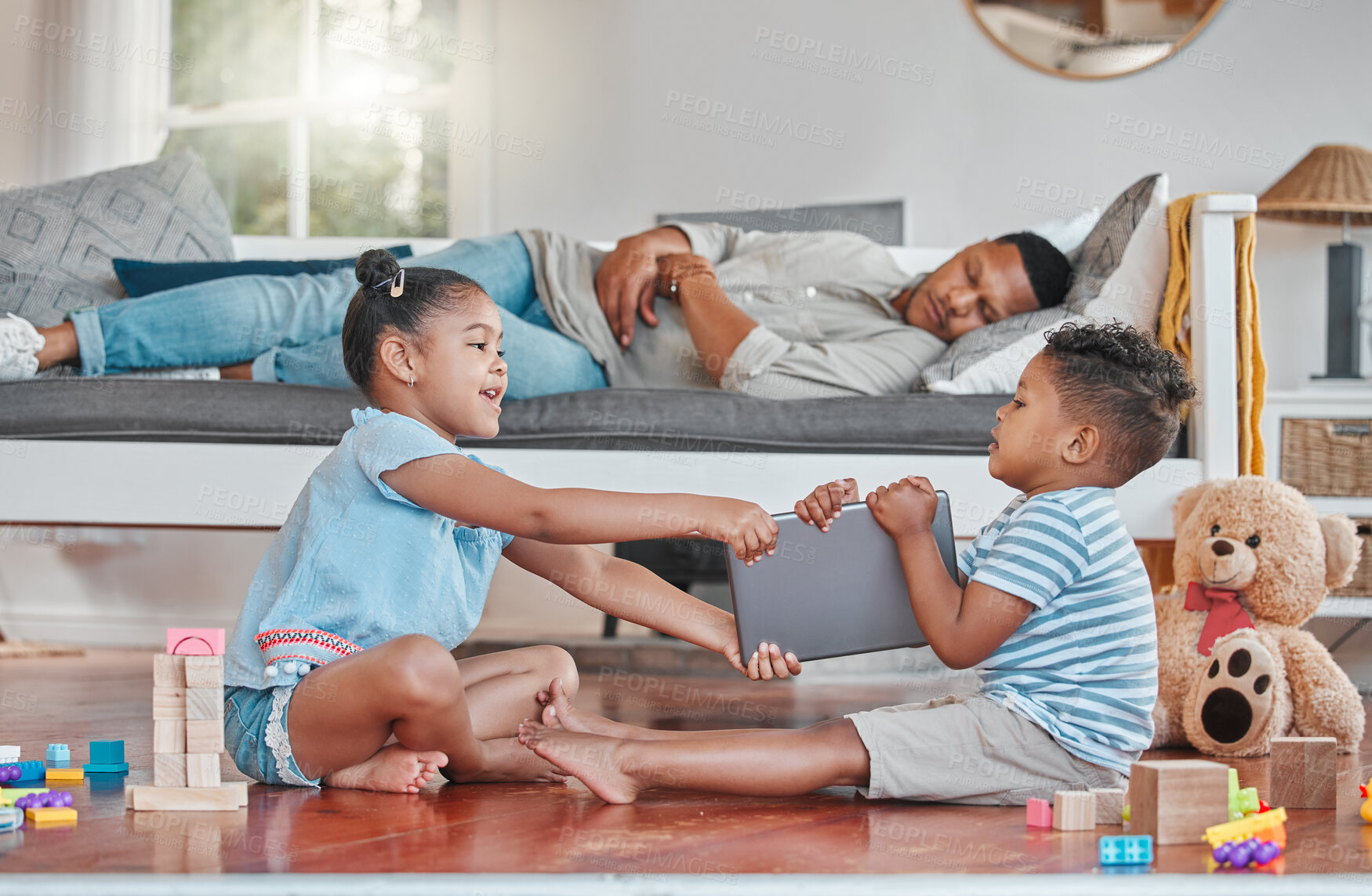 Buy stock photo Shot of two siblings fighting over a digital tablet on the floor while their dad sleeps on the couch at home