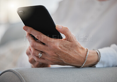 Buy stock photo Cropped shot of an unrecognizable senior woman sending a text while relaxing in her living room at home