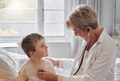 Buy stock photo Shot of a doctor examine a little boy with a stethoscope in bed at home