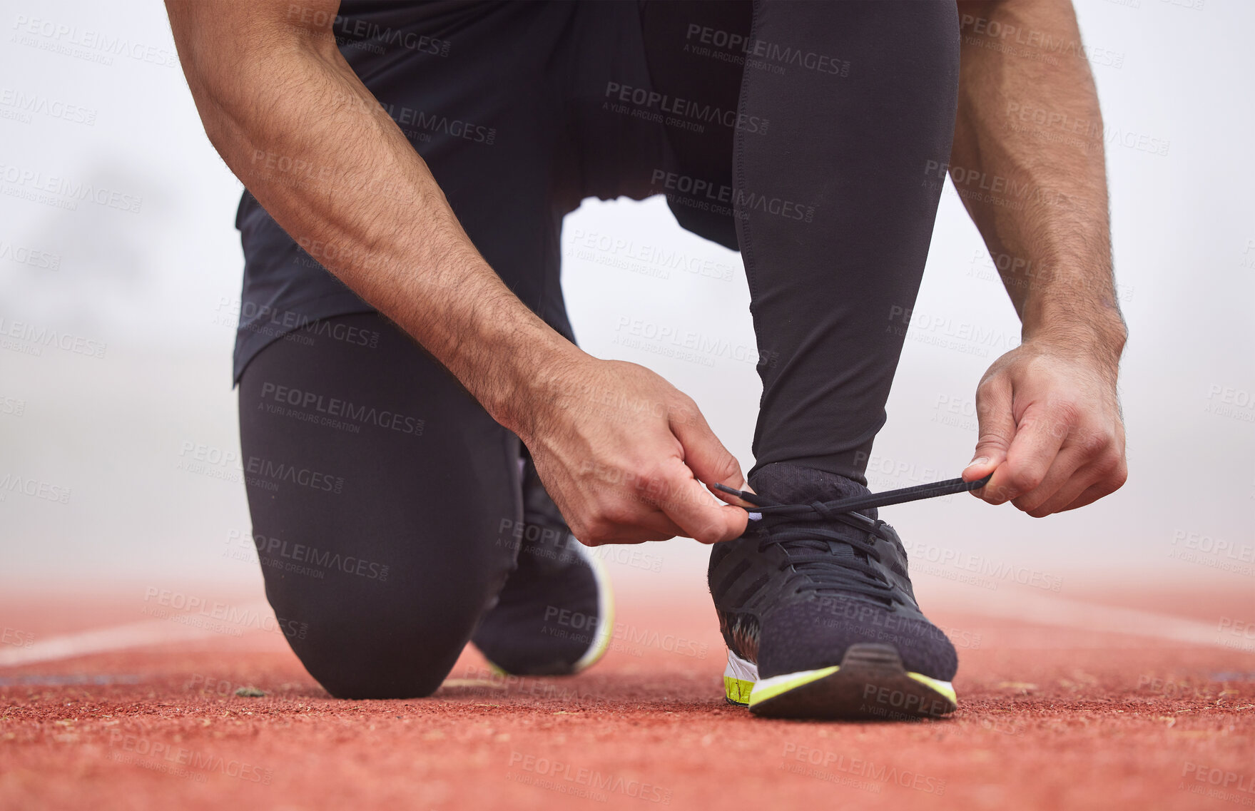 Buy stock photo Cropped shot of an unrecognizable male athlete tying his laces out on the track
