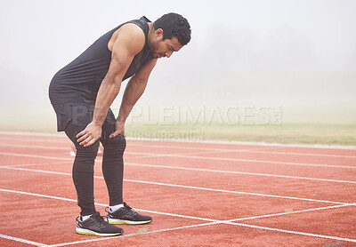 Buy stock photo Full length shot of a handsome young male athlete hunched over on the track after a race