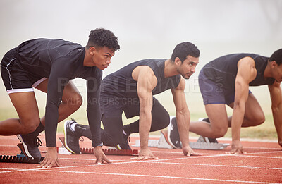 Buy stock photo Cropped shot of three handsome young male athletes starting their race on a track