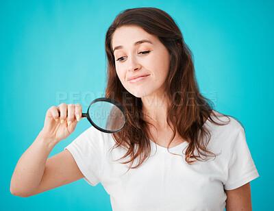 Buy stock photo Studio shot of an attractive young woman posing with a magnifying glass against a blue background