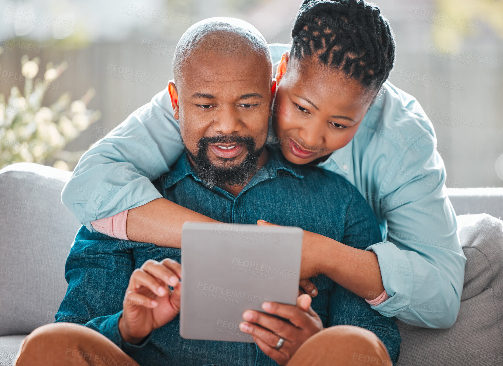 Buy stock photo Shot of a mature woman hugging her husband while he uses a digital tablet