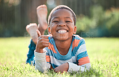 Buy stock photo Thumbs up, portrait of black boy and lying on grass in a nature park with a lens flare. Good news or thank you,  success or winner and happy or excited young male child relaxing on a lawn outdoors