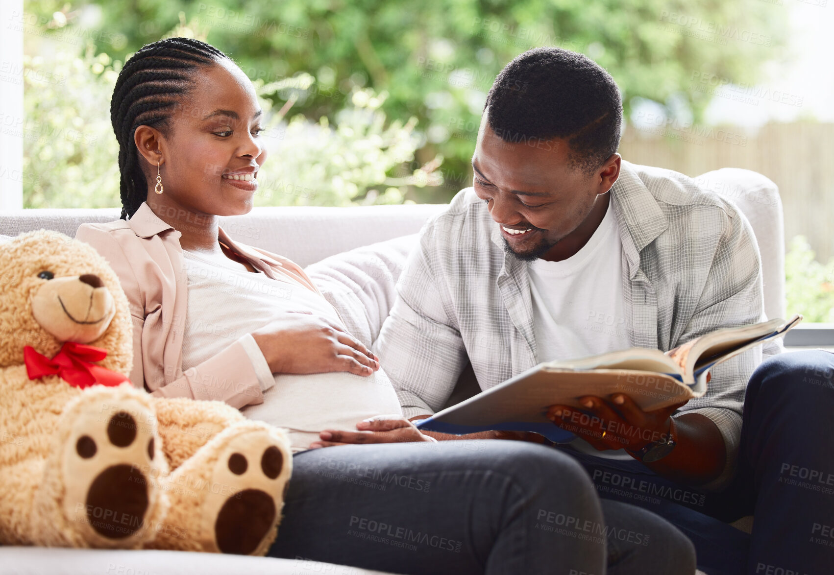 Buy stock photo Cropped shot of a handsome young man reading a book to pregnant wife's belly while sitting on the sofa at home