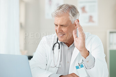 Buy stock photo Shot of a senior doctor sitting in his clinic and using his laptop for a conference call