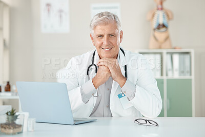 Buy stock photo Shot of a senior doctor sitting alone in his clinic and using his laptop