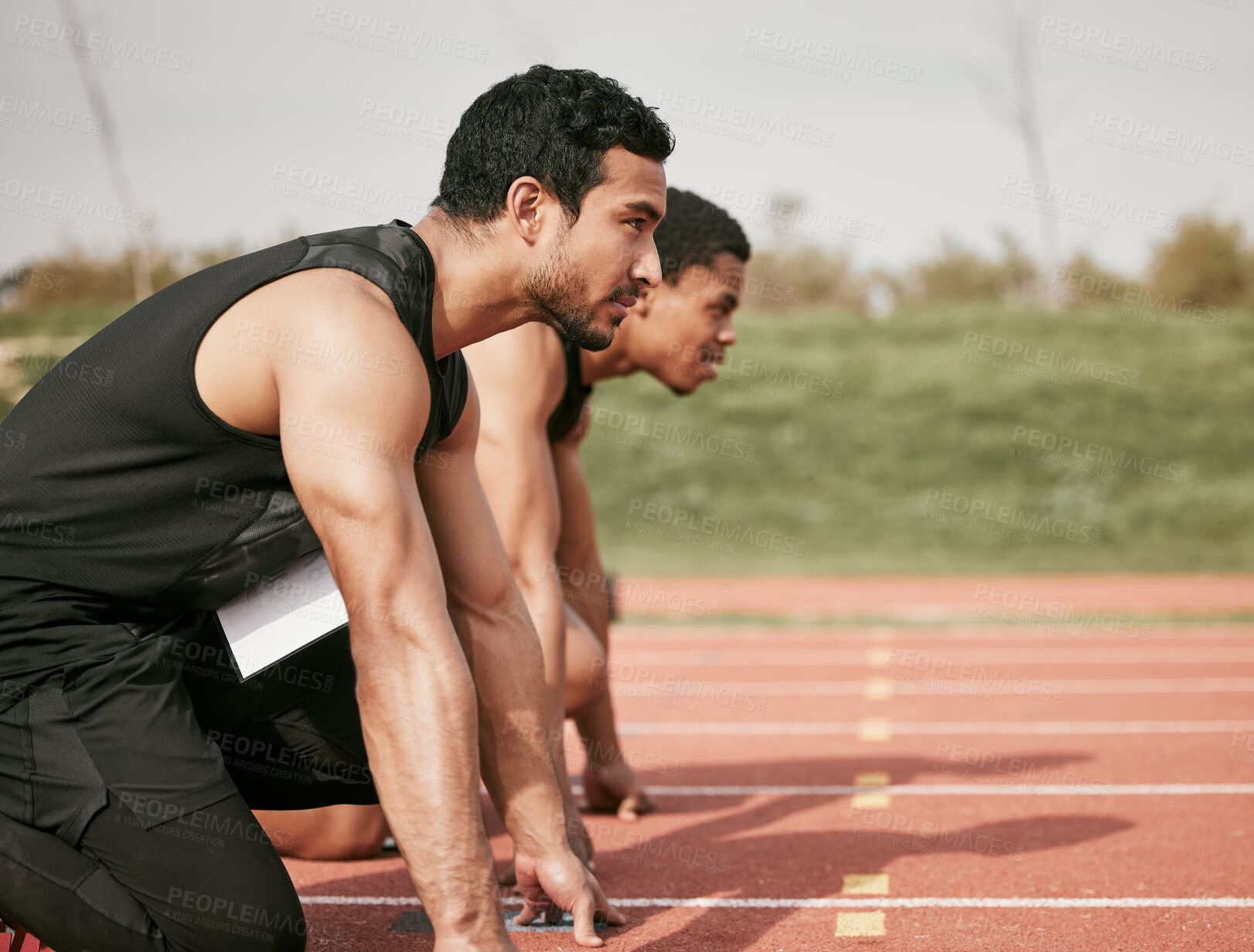 Buy stock photo Cropped shot of two handsome young male athletes starting their race on a track