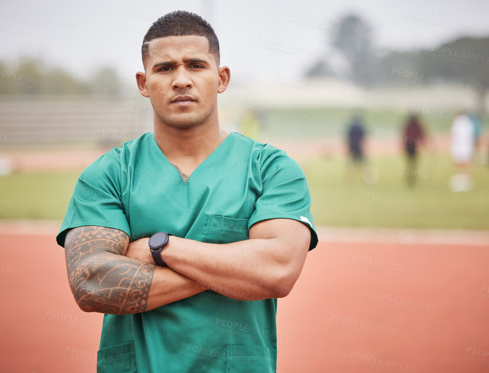 Buy stock photo Cropped portrait of a handsome young male paramedic standing with his arms folded on a track outside