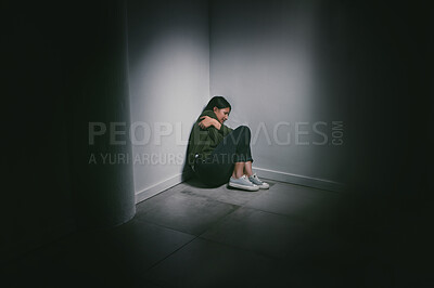 Buy stock photo Shot of a young woman sitting in the corner of a dark room