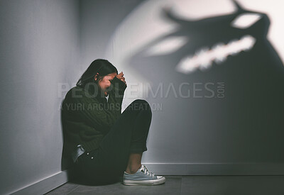 Buy stock photo Shot of a young woman sitting in the corner of a dark room with a scary figure on the wall