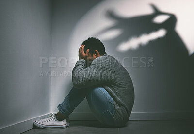 Buy stock photo Shot of a young man sitting in the corner of a dark room with a scary figure on the wall
