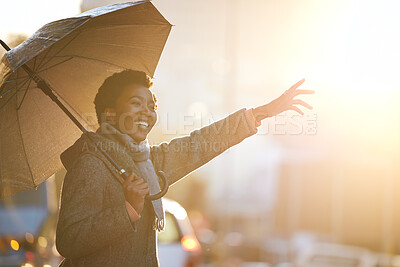 Buy stock photo Shot of a young businesswoman using an umbrella and gesturing to order a cab against an urban background