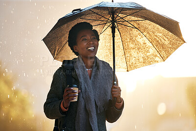 Buy stock photo Shot of a young businesswoman using an umbrella and having coffee while going for a walk in the rain against an urban background