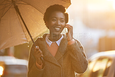 Buy stock photo Shot of a young businesswoman using an umbrella and a smartphone while going for a walk in the rain against an urban background