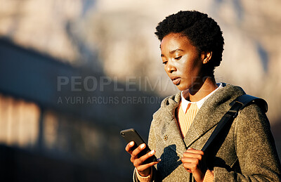 Buy stock photo Shot of a young businesswoman using a smartphone while going for a walk on a rainy day in the city