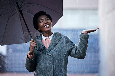 Buy stock photo Shot of a young businesswoman using an umbrella to cover with while going for a walk in the rain against an urban background