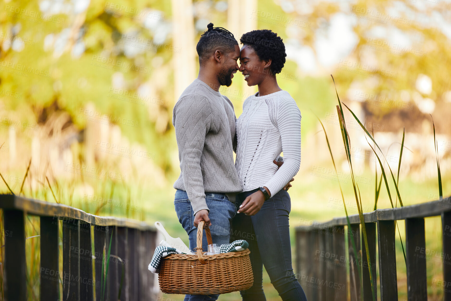 Buy stock photo Black couple, love and picnic at park with basket for anniversary date, honeymoon celebration and romance with smile. People, embrace and happy on bridge in nature with support, care and holiday fun