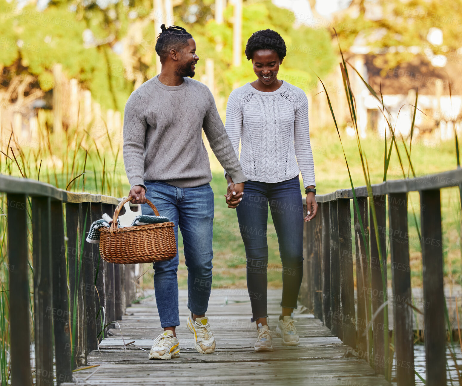 Buy stock photo Couple, holding hands and picnic at park with basket for anniversary date, honeymoon celebration and romance with smile. Black people, love and happy on bridge with support, care and holiday fun