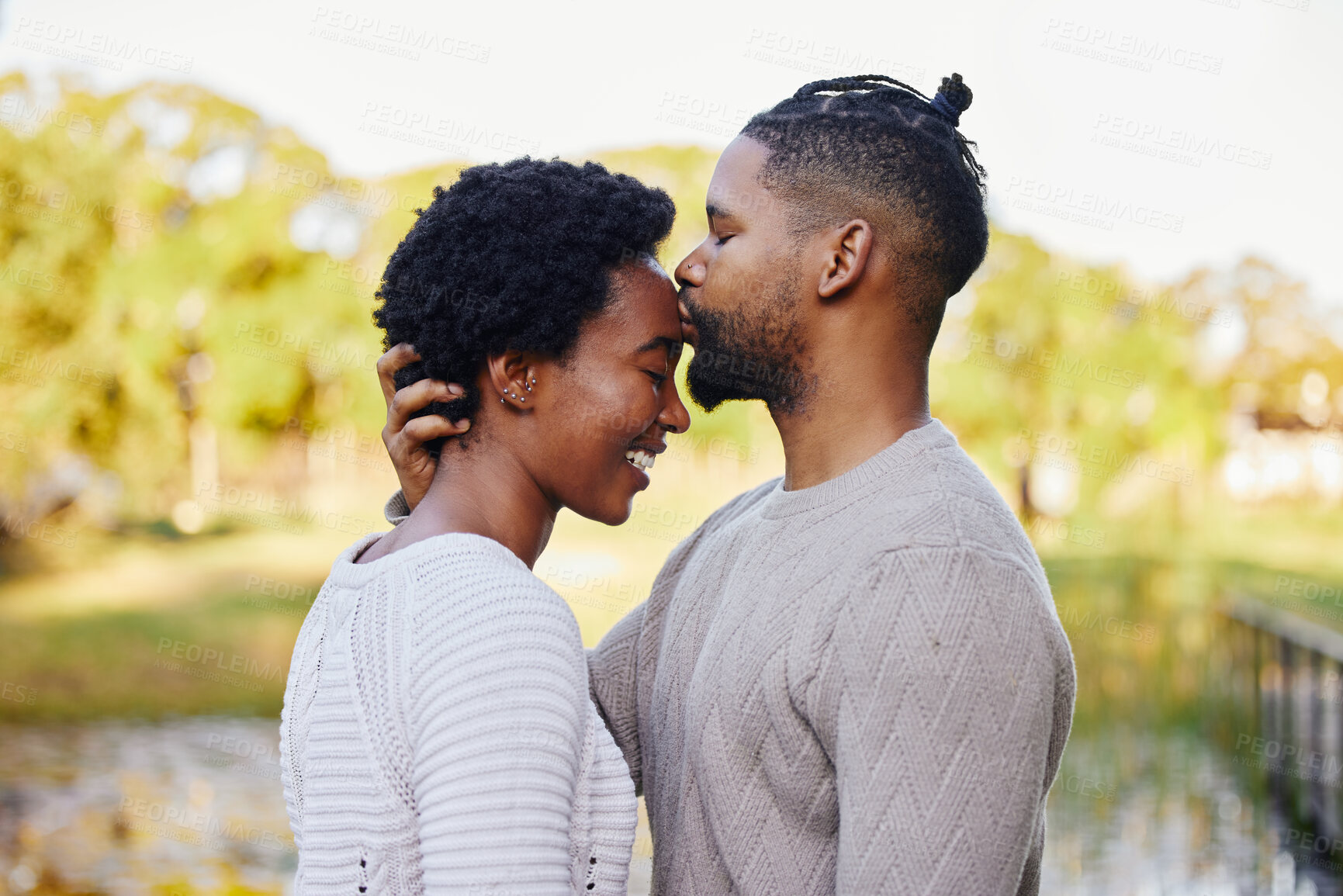 Buy stock photo Black couple, happy and forehead kiss by lake for love in park with smile, trees and nature on summer holiday. Man, woman and support or trust outdoor with sunshine, date and vacation in morning