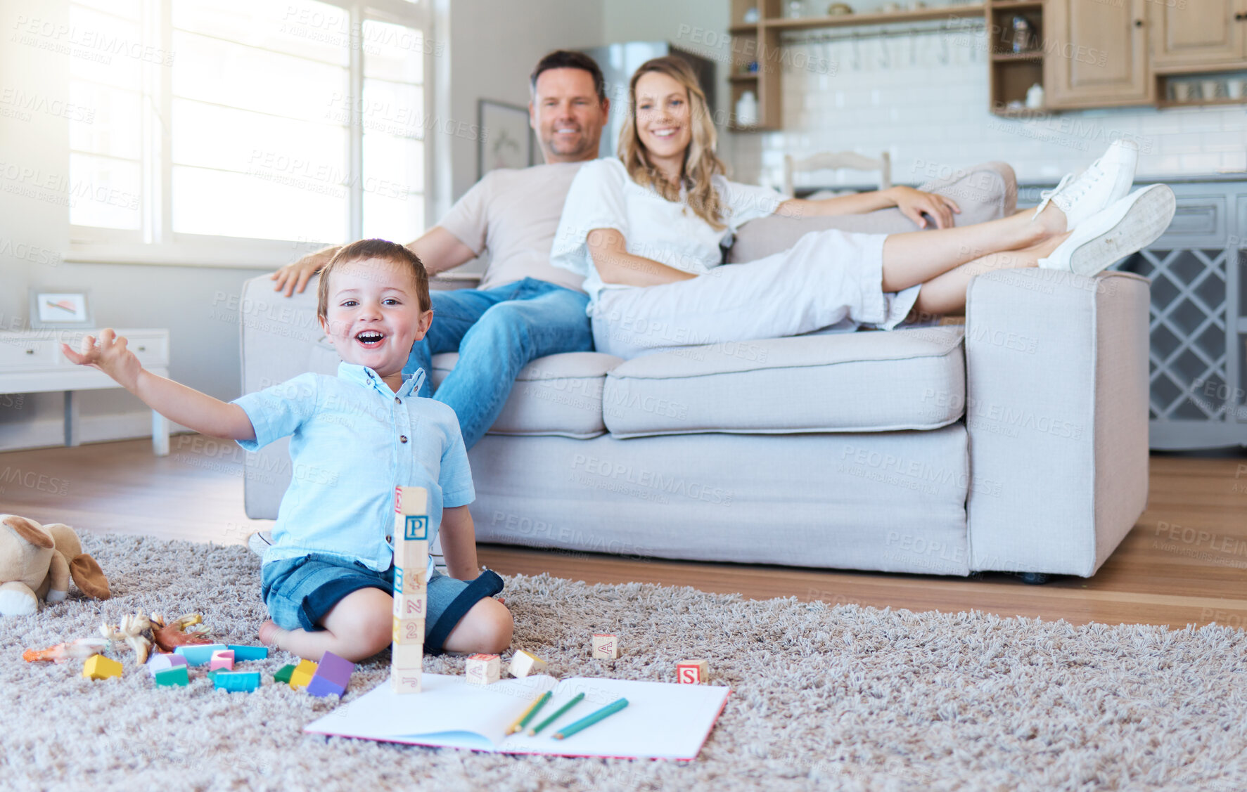 Buy stock photo Shot of a boy playing with his toys while his parents sit on the couch at home