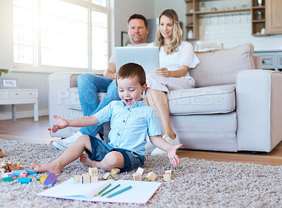 Buy stock photo Shot of a boy playing with his toys while his parents sit on the couch  and use a laptop at home