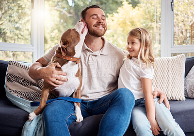 Buy stock photo Shot of a handsome young man sitting on the sofa at home and bonding with his daughter and dog