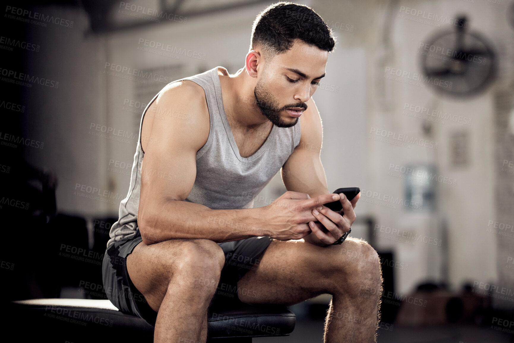 Buy stock photo Shot of a muscular young man using a cellphone in a gym