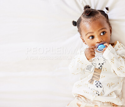 Buy stock photo High angle shot of an adorable baby girl sucking on a dummy while lying on a bed at home