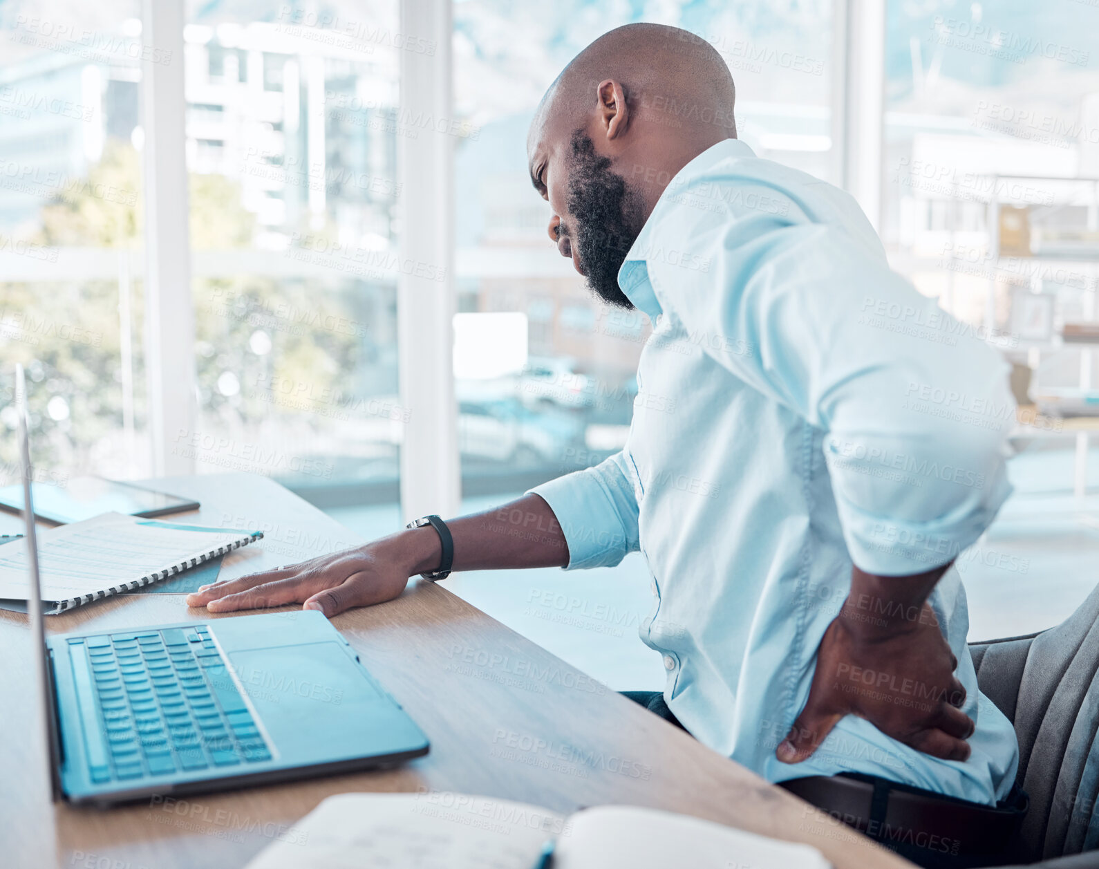 Buy stock photo Businessman, laptop and pain in back in office for tired with muscle injury, job stress and poor posture. Black male consultant, tech and body fatigue by desk with spine problem, strain and scoliosis