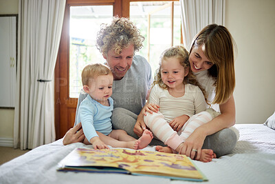Buy stock photo Shot of a young family happily bonding while reading a book together in bed at home